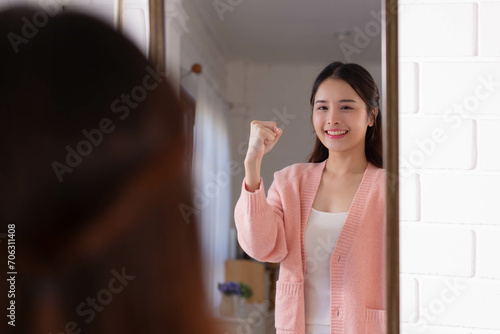 Smiling beautiful asian woman looking at herself in the bathroom mirror at home.