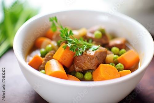 close-up of beef stew with carrots and peas in white bowl
