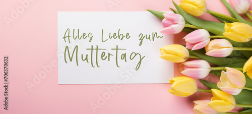 Alles Liebe zum Muttertag Feiertag Grußkarte - Weisses Papier, Rahmen mit deutschem Text und Tulpen auf pinkem Tisch Hintergrund, Draufsicht