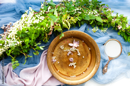 Fancy hand mirror and bowl of water among leaves and flowers prepared for skin care procedure