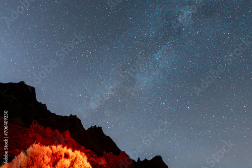 Beautiful night photograph with a clear and starry sky, with the Milky Way and an illuminated and silhouetted mountain in the Teide National Park, in Tenerife, Canary Islands, Spain, Europe