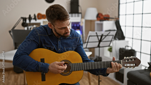 Captivating young hispanic man engrossed in playing a classic guitar melody at a music studio indoors, showcasing his musical talent