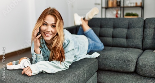 Young caucasian woman talking on the smartphone lying on sofa at home