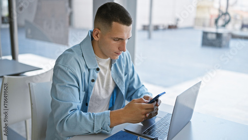 Handsome hispanic man studying with laptop and smartphone in modern university library.