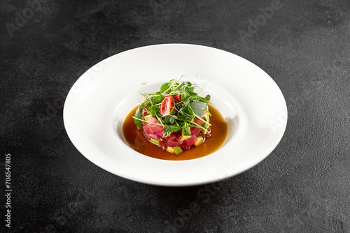 Tuna and avocado tartare topped with microgreens and cherry tomatoes, served in a white bowl