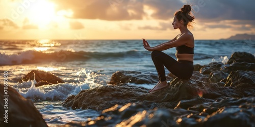 A fitness enthusiast, a young woman, finds serenity in her yoga practice, savoring the gentle caress of the wind and inhaling the crisp sea breeze as she balances on the rocky beach
