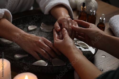Woman receiving hand massage in spa salon, closeup. Bowl of water and flower petals on table