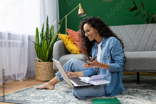 Young beautiful woman sitting on the floor at home in the living room, student studying remotely, using laptop to watch webinar and video course, online call consultation with teacher.