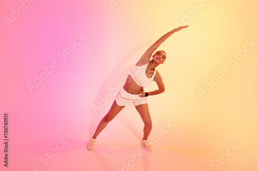 A joyful woman with a shaved head stretches side to side, wearing a white sports bra and shorts