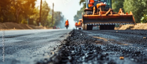 Transport workers in bright orange reflective vests prepare old pavement for repairs and remove road debris into a grader bucket after clearing old asphalt from the road Copy space