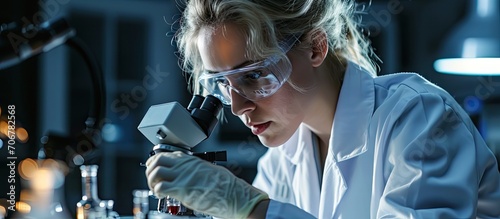 My analysis Content promising blond scientist holding blood test tubes and wearing a uniform and medical gloves while sitting near a microscope. with copy space image. Place for adding text or design