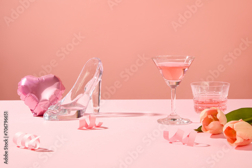 A heart-shaped balloon, glass high heel, tulip flowers and wine glasses arranged on pink surface. For valentine or anniversary party
