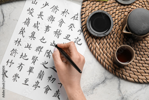 Female hand with Asian hieroglyphs, nib pen, ink and cup of tea on light background, closeup. International Haiku Poetry Day