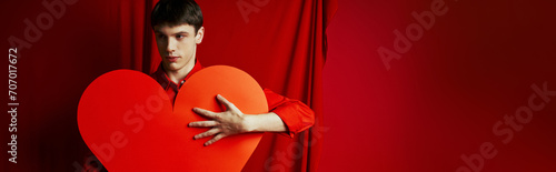 young man in shirt embracing large heart shaped carton on red background, Valentines day banner