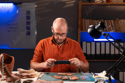 Archaeological concept. Male archaeologist doing research, uses smartphone and share discovery ancient civilization cultural artifacts on social media