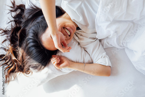 Attractive happy Asian woman lies on a white linen bed in the morning