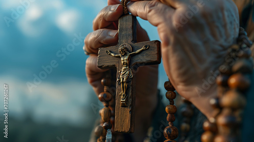 Close-up of the hands of an old man holding a rosary and a cross.