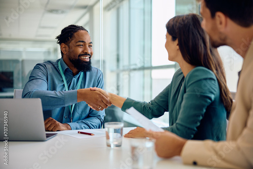 Happy black financial advisor handshaking with his clients during meeting in office.
