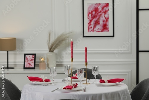 Color accent table setting. Glasses, plates, burning candles and pink napkins on table in dining room