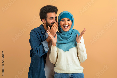 Delighted arab muslim couple sharing joyful secret, man whispering into woman's ear