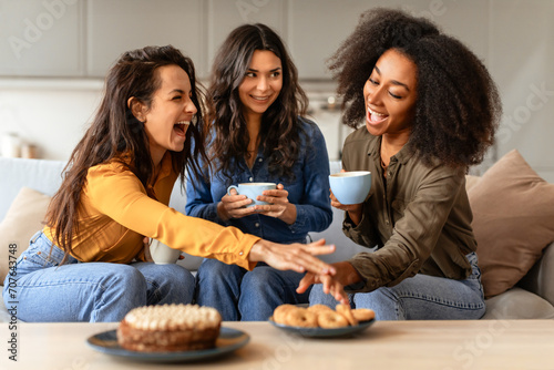 Three joyful multiethnic friends ladies share laughter over coffee indoors