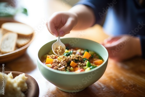 kids hand dipping bread into bowl of minestrone