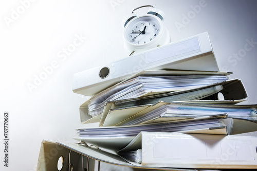 Alarm clock on stacked ring binders against a gray background threatened to deadline ultimatum, business concept for time management and work overload, view from below, copy space