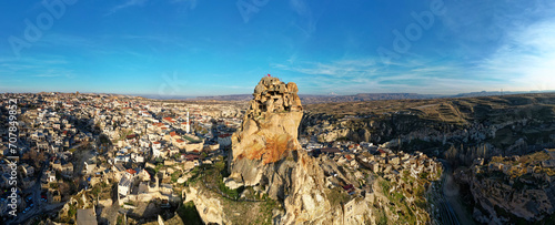 Aerial drone view of the Ortahisar Castle in Cappadocia, Turkey with the snow capped Mount Erciyes in the background. People enjoying the view from the top of the castle. 