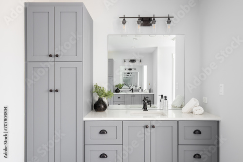 A renovated modern farmhouse bathroom detail with grey cabinets, decorations on a white marble countertop, and rubbed bronze faucet.