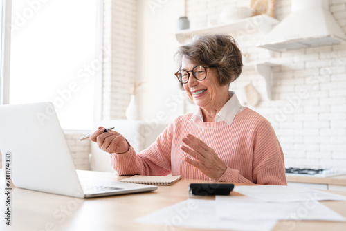 Emotional winner old lady woman elderly senior grandmother receiving money pension loan budget transfer cashback on bank account, calculating income at home kitchen