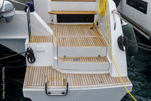 Stern of super luxury yacht berthed in marina. Teak deck on stern of sailing boat. Teak stairs ladder on motor boat. Aft part. Yachting concept.