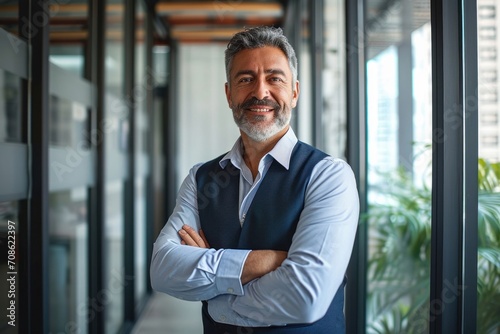 Happy confident mature latin business man standing in office hall, portrait. Smiling mid aged older corporate manager, successful executive investor looking at camera with arms crossed, Generative AI