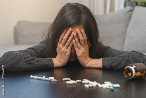 Anti, drug addict asian young woman hand cover face in front of pills, medicament with narcotic syringe on table, abuse overdose. Sick pain of health, unhealthy people. Suicide depressed or despair.