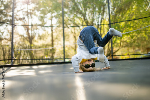 Cute little boy jumping on a trampoline in a backyard on warm and sunny summer day. Sports and exercises for children.