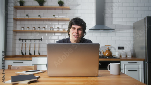 Happy man sitting in the kitchen having video call conversation through using laptop computer. Share news, talk to family, enjoy webchat virtual meeting 