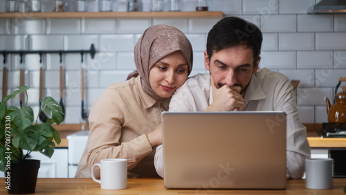 Newly married couple sitting in the kitchen using laptop saddened by the news, the loss, the wife consoles the husband. Disappointed bad news, loss negative result 