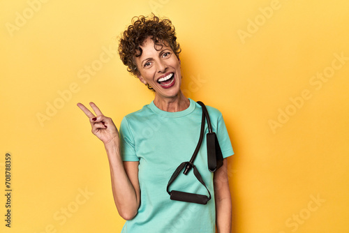 Sportswoman with resistance bands on yellow joyful and carefree showing a peace symbol with fingers.