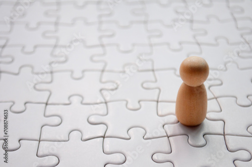 A wooden doll on white jigsaw puzzle. Loneliness concept