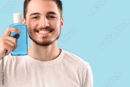 Handsome young man with bottle of mouthwash on blue background. Dental care concept