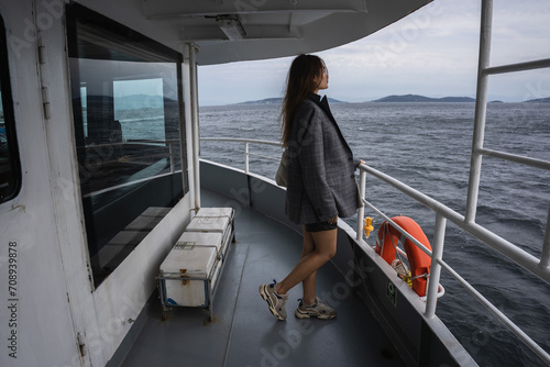 Istanbul. An Asian girl in a man's jacket is sailing on a ferry in Istanbul in cloudy weather, standing on the upper deck with a lifebuoy in the background