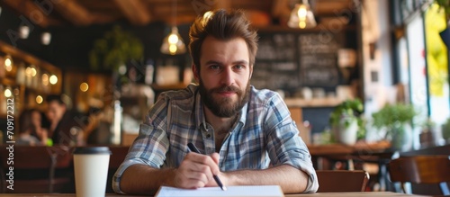 Bearded man taking notes in indoor cafe setting.