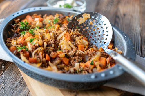 Minced meat pan with cabbage and vegetables in a roasting pan on wooden table