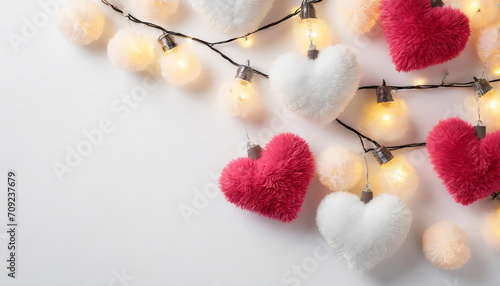 Top view of fluffy heart shaped toys light bulb garland and soft pompons on light gray background with copy space