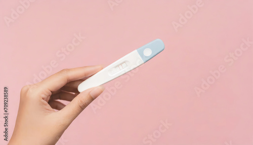 Young woman hand holding pregnancy test on pastel pink background with copy space