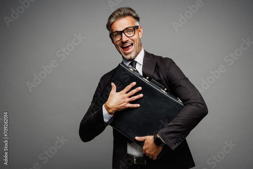 Smiling adult happy successful employee business man corporate lawyer wear classic formal black suit shirt tie work in office hold in hand briefcase isolated on plain grey background studio portrait.
