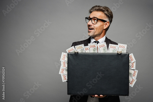 Adult rich employee business man corporate lawyer wearing classic formal black suit shirt tie work in office hold cash money in case for dollar banknotes look aside isolated on plain grey background.