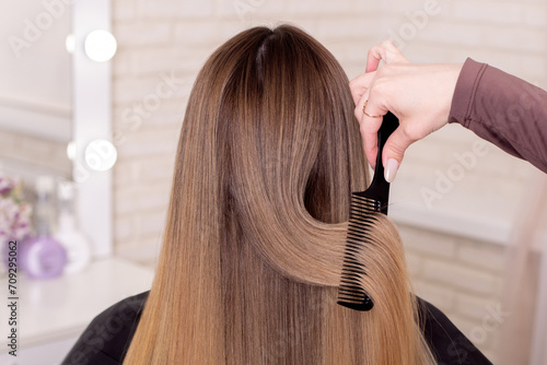 Hairdresser's hand brushing long natural blonde hair in beauty salon