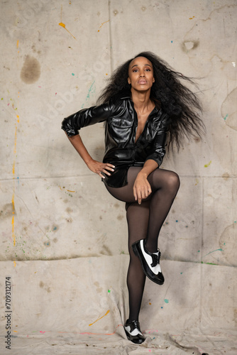 Tall African American Woman in black stockings, leather shirt and long hair poses before a canvas drop in a downtown studio