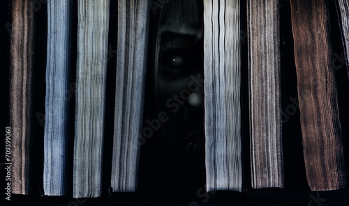 Photo of scary haunted ghost or monster face peeking out between books.