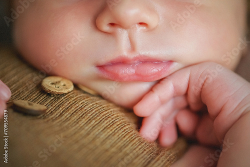 lose-up of a newborn's face. Lips, nose, pen. A newborn baby sleeps sweetly on a pillow. Baby in a brown bodysuit and a brown hat. Younger brother. Portrait of a newborn. The baby gently touches his 